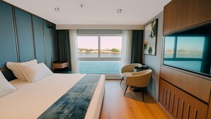 Ein modernes Hotelzimmer mit einem großen Bett, einer Sitzecke mit einem Sessel, einem Fernseher und Blick auf das Wasser.