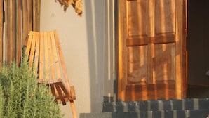 A wooden door with a textured surface, a wooden chair, and a small plant in the foreground. - Sibebe Hills Vista (Mbabane)