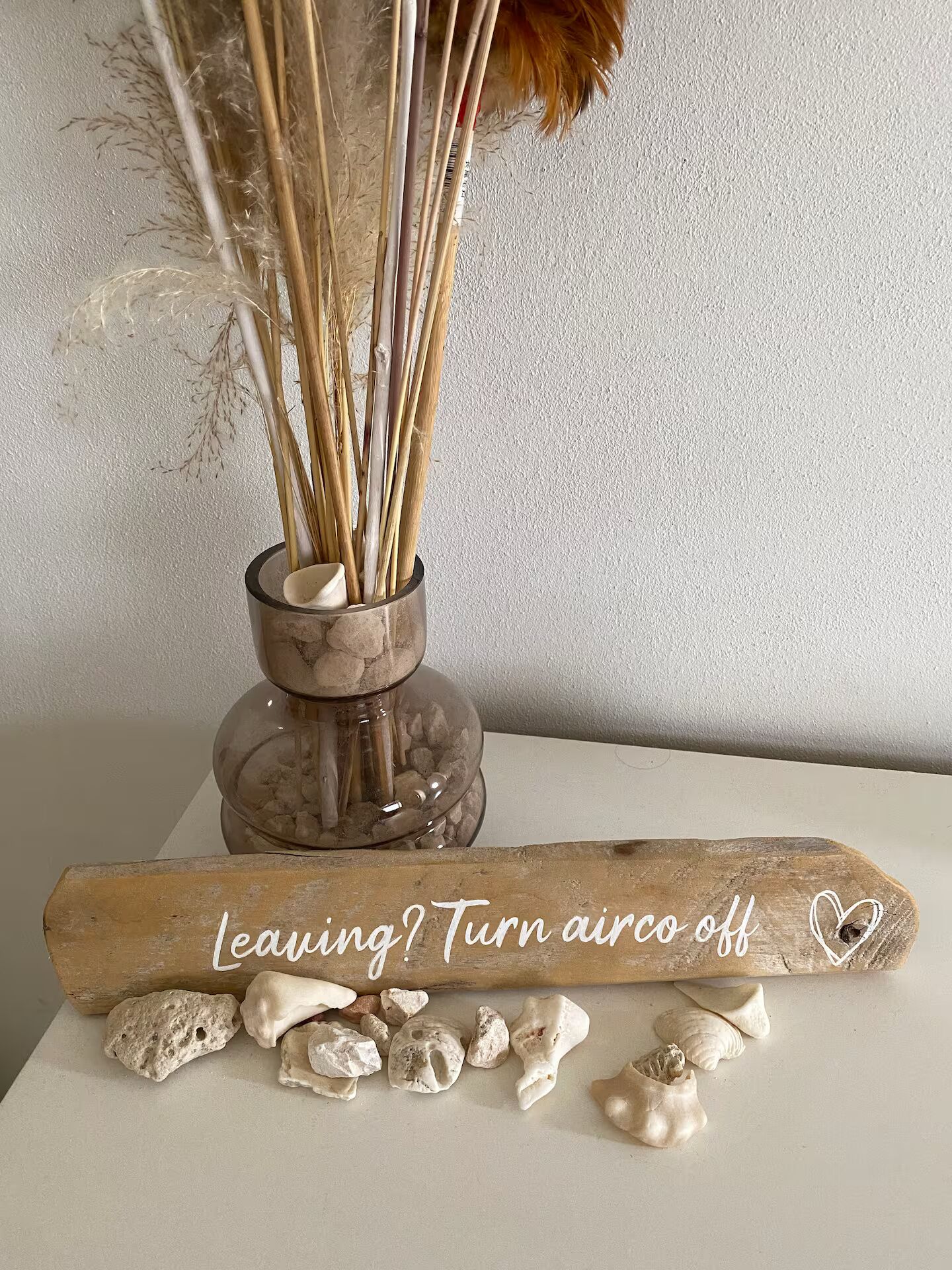 Een decoratieve opstelling met een vaas gedroogde rietstengels en een houten bord met tekst.
