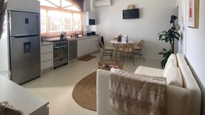 A modern kitchen with a built-in oven and a dining area with a round table and chairs. - Palm Beach Vacaysuites - Coconut Suite - Top Floor (Noord)