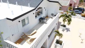 A modern two-story house with a balcony, outdoor seating, and potted plants. - Palm Beach Vacaysuites - Coconut Suite - Top Floor (Noord)