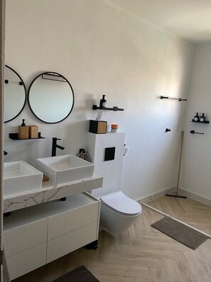 A modern bathroom with two sinks, a toilet, and a shower. - Palm Beach Vacaysuites - Coconut Suite - Top Floor (Noord)