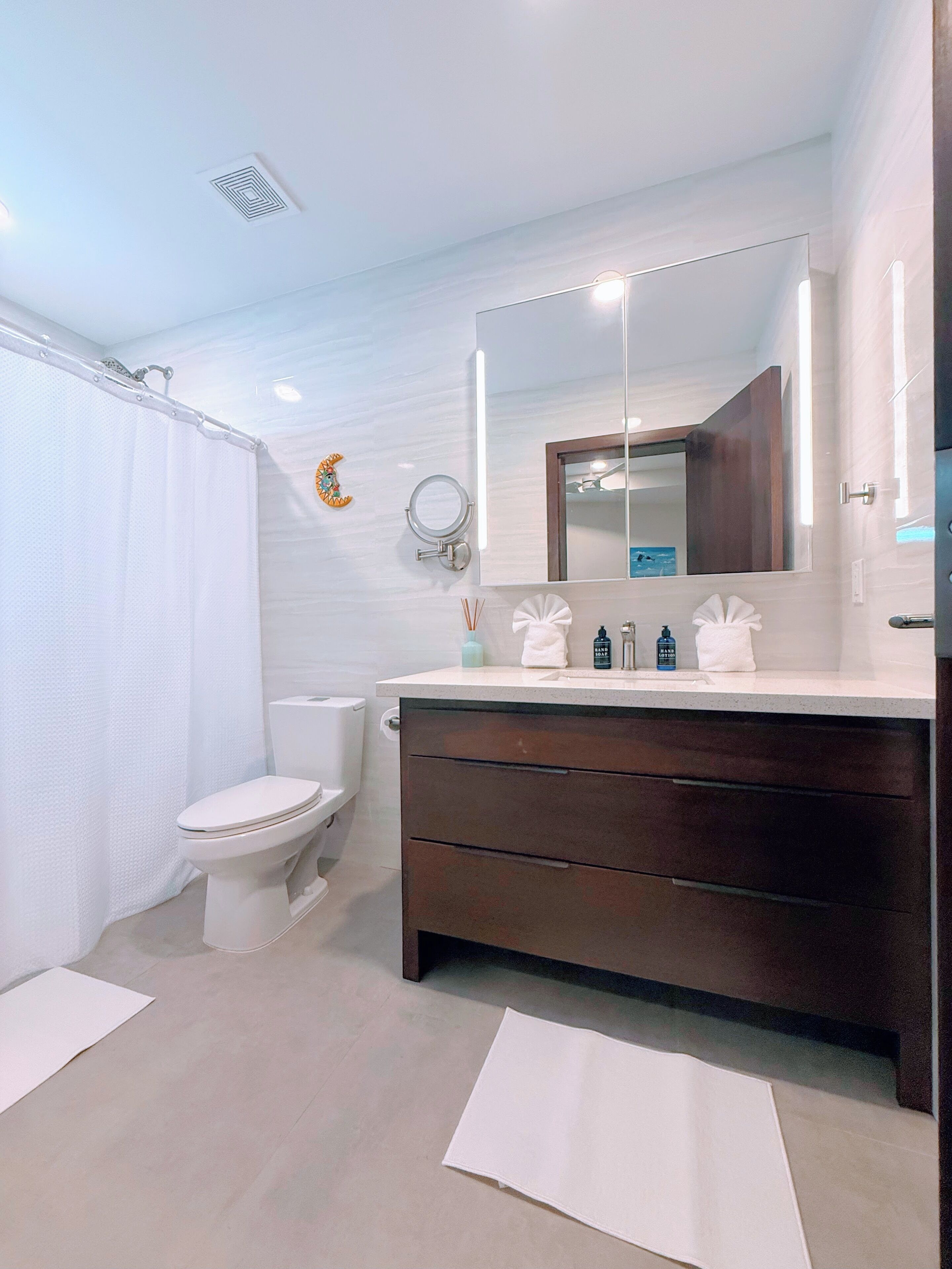 A modern bathroom with a white toilet, a dark wooden vanity, a large mirror, and a shower curtain.