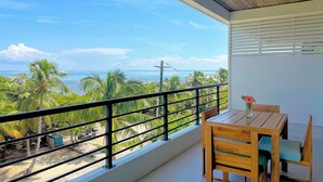 A balcony with a view of the ocean, a wooden table with chairs, and a flower vase. - Hibisco Belize (San Pedro)