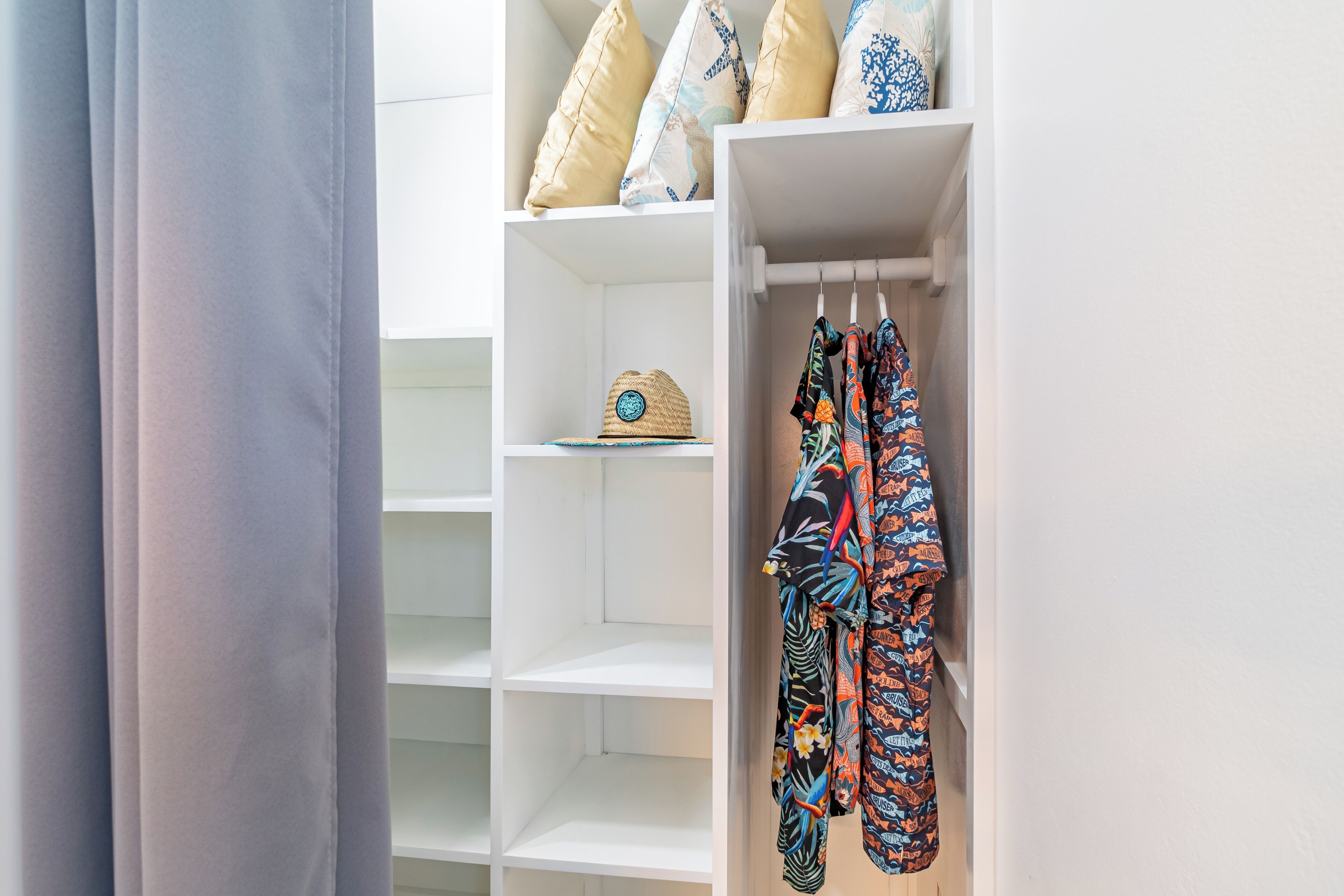 A white closet with shelves and hanging space, a woven hat, and patterned garments.
