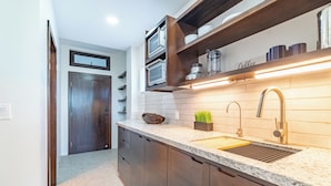 A modern kitchen with dark wooden cabinets, a granite countertop, a double sink, and built-in appliances. - Hibisco Belize (San Pedro)