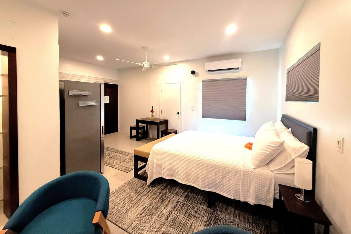 A modern hotel room with a bed, a desk, a chair, and an air conditioning unit.