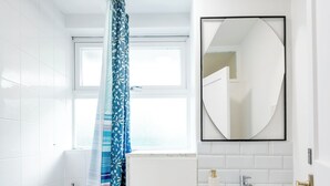 A modern bathroom with a bathtub, a sink, and a mirror. - Cozy 2 bedroom London flat in heart of Victoria (London)