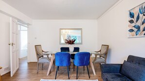 A dining area with a table, two blue chairs, a grey sofa, and a floral rug. - Cozy 2 bedroom London flat in heart of Victoria (London)