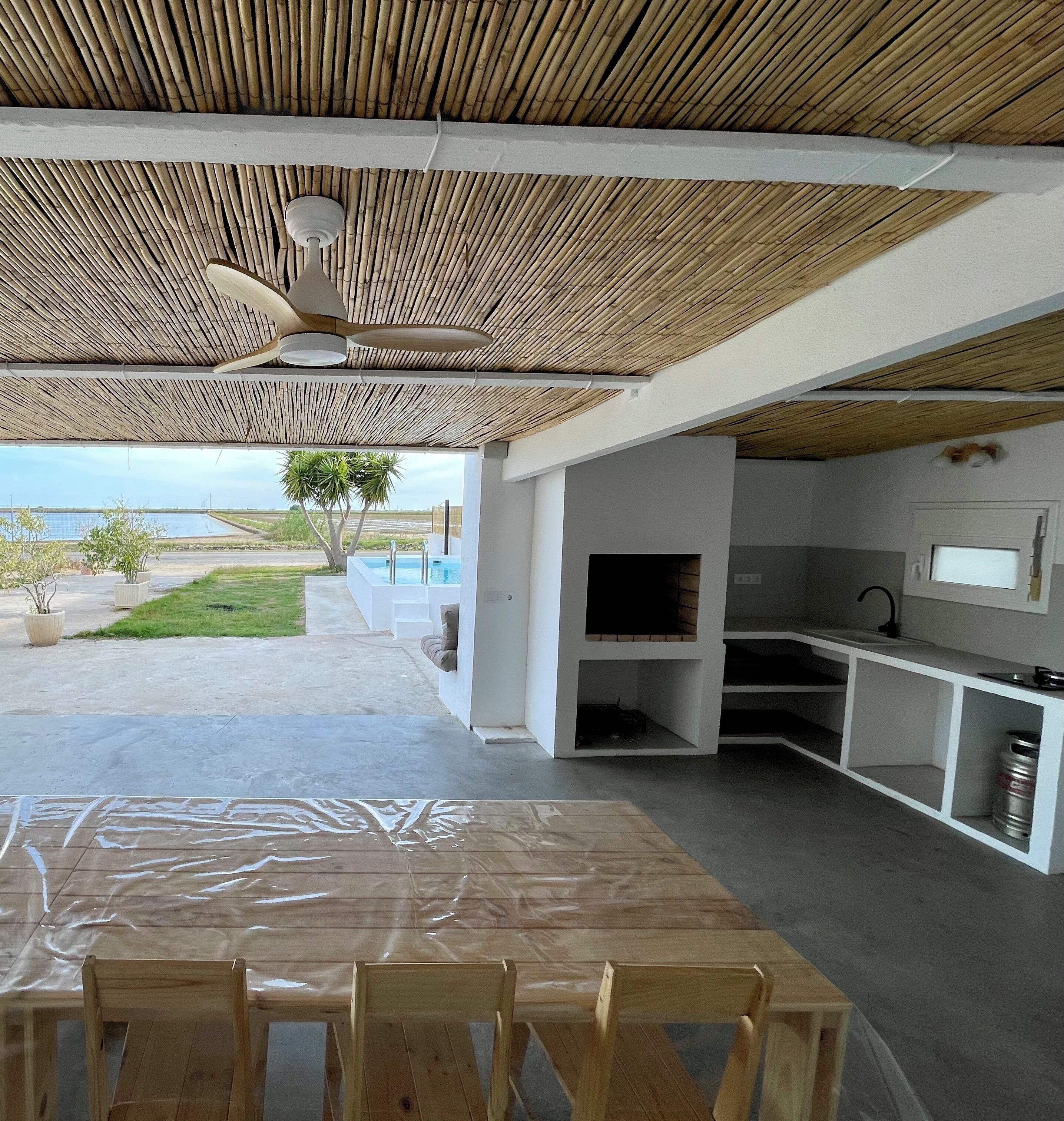 An outdoor kitchen area with a table and chairs, a ceiling fan, and a view of the sea.