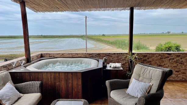 A hot tub with a view of a rice field. There are wicker chairs and a table with a plant.