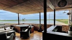 A covered outdoor seating area with a view of a water body and fields.