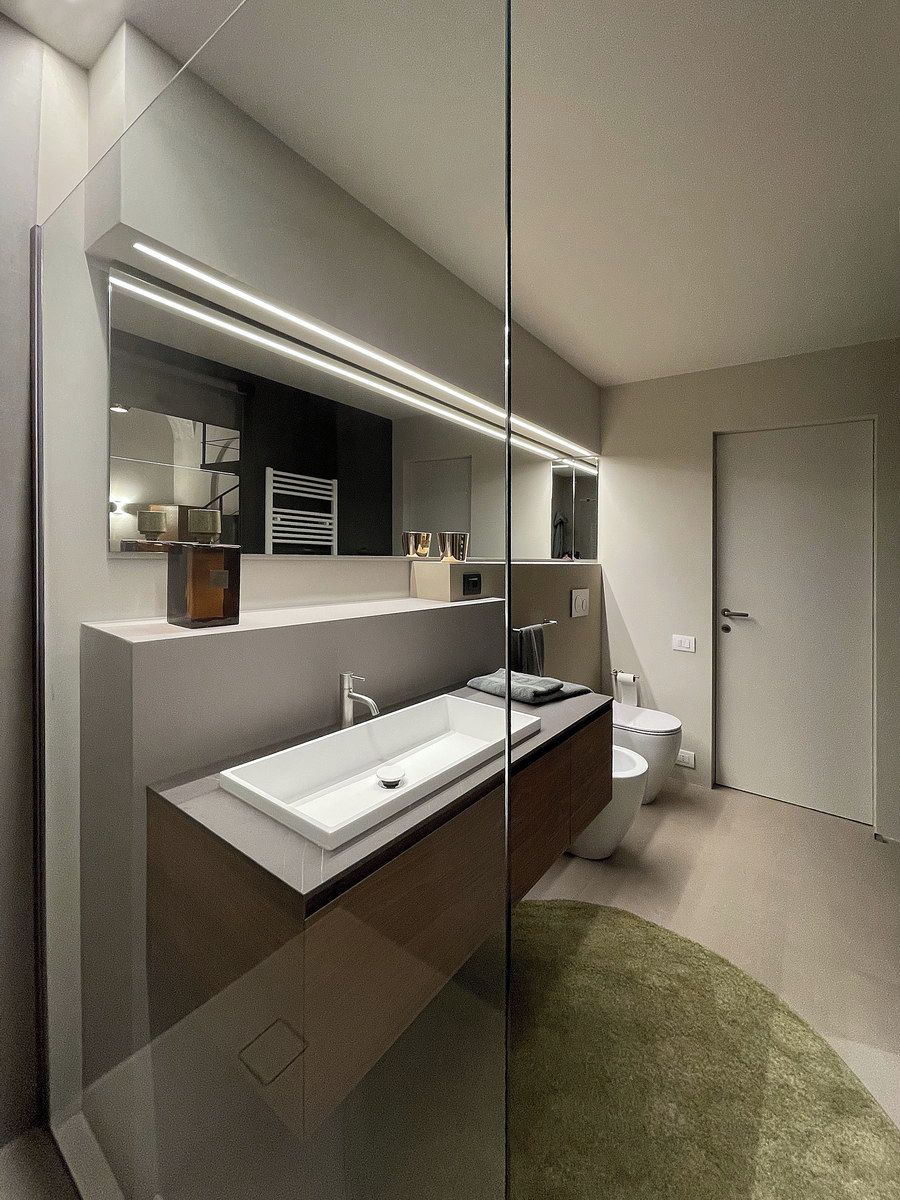 Un baño moderno con un espejo grande, un lavamanos blanco y un inodoro.