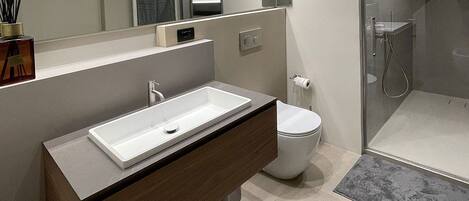 Un baño moderno con un espejo grande, un lavamanos blanco, un inodoro y una zona de ducha.