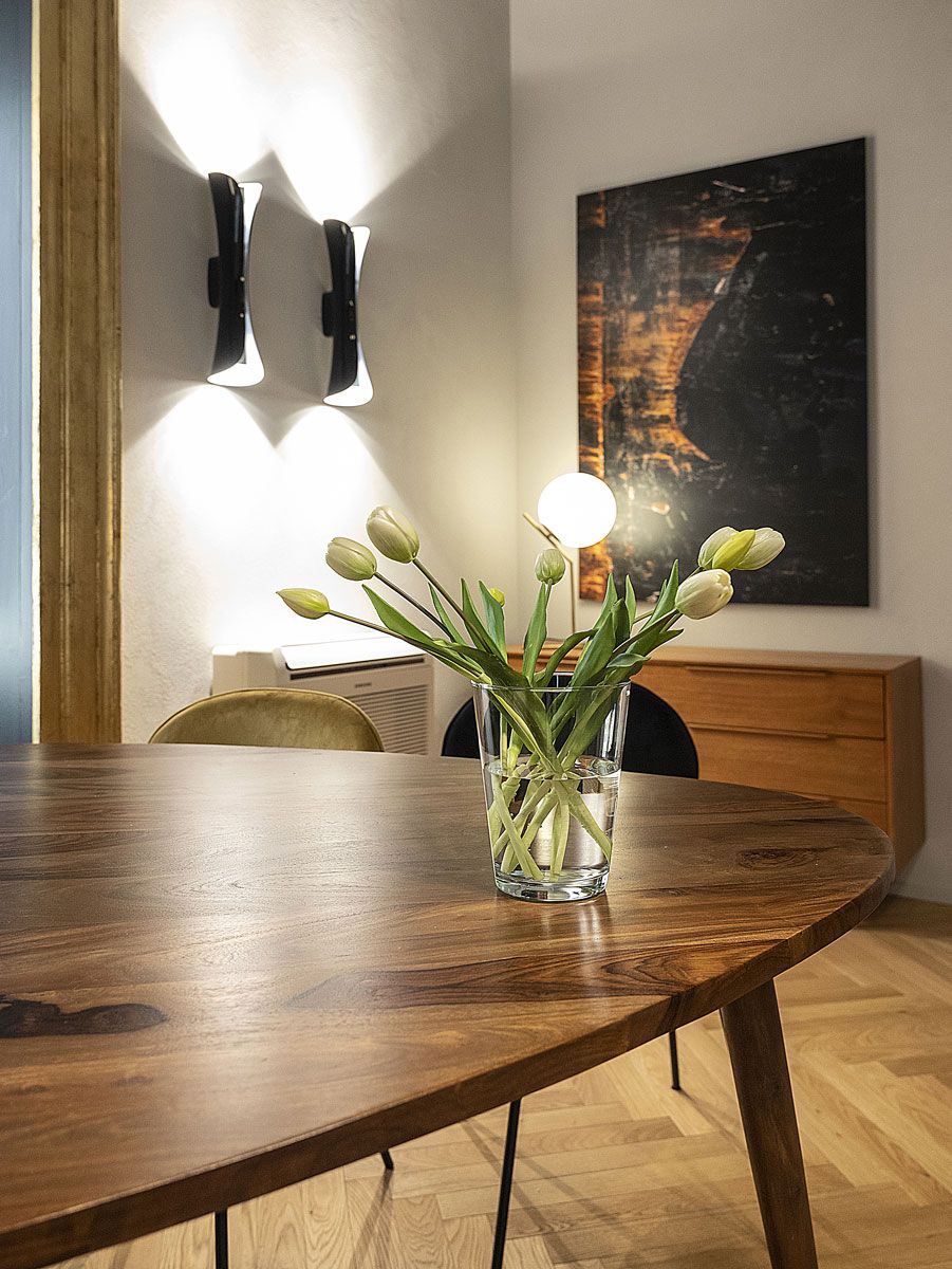 A dining table with a glass vase containing tulips, a wall-mounted light fixture, and a painting on the wall.
