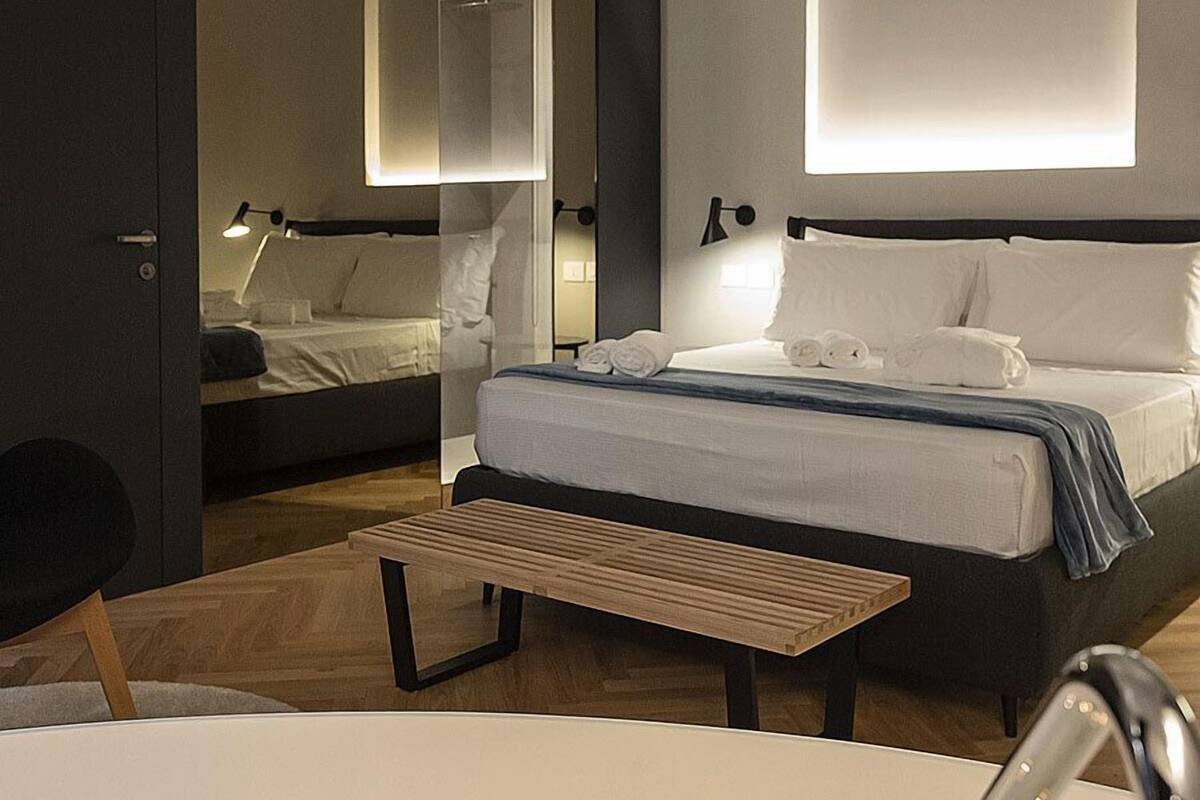 Quarto de hotel moderno com uma cama grande, uma mesa de cabeceira, um espelho e um banheiro com banheira.