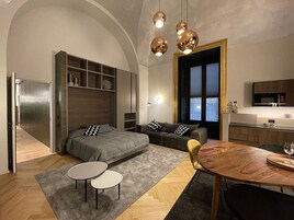 A modern bedroom with a built-in wardrobe, a sofa bed, a dining table, and a kitchen area.