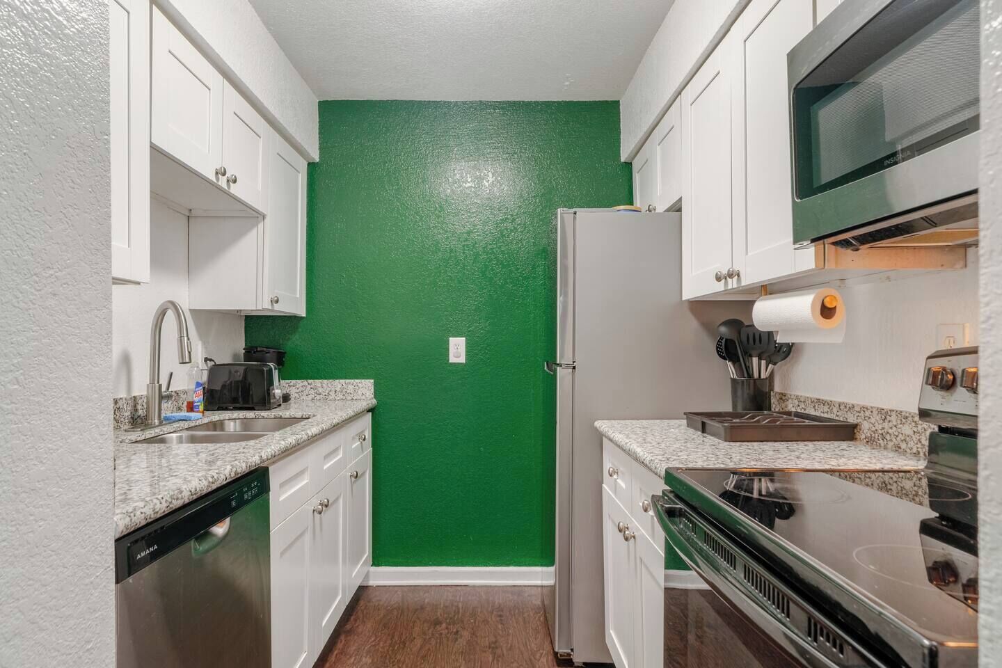 Une cuisine compacte avec des meubles blancs, un mur vert, un four à micro-ondes, une cuisinière et un lave-vaisselle.
