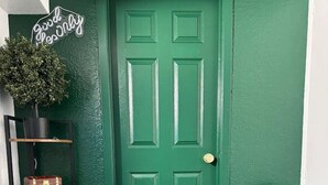 A green door with a sign above it, a round green rug, a chair, and a shelf with decorative items. - Pool Table  Luxury 1Bed Apt in Downtown & Heights (Houston)
