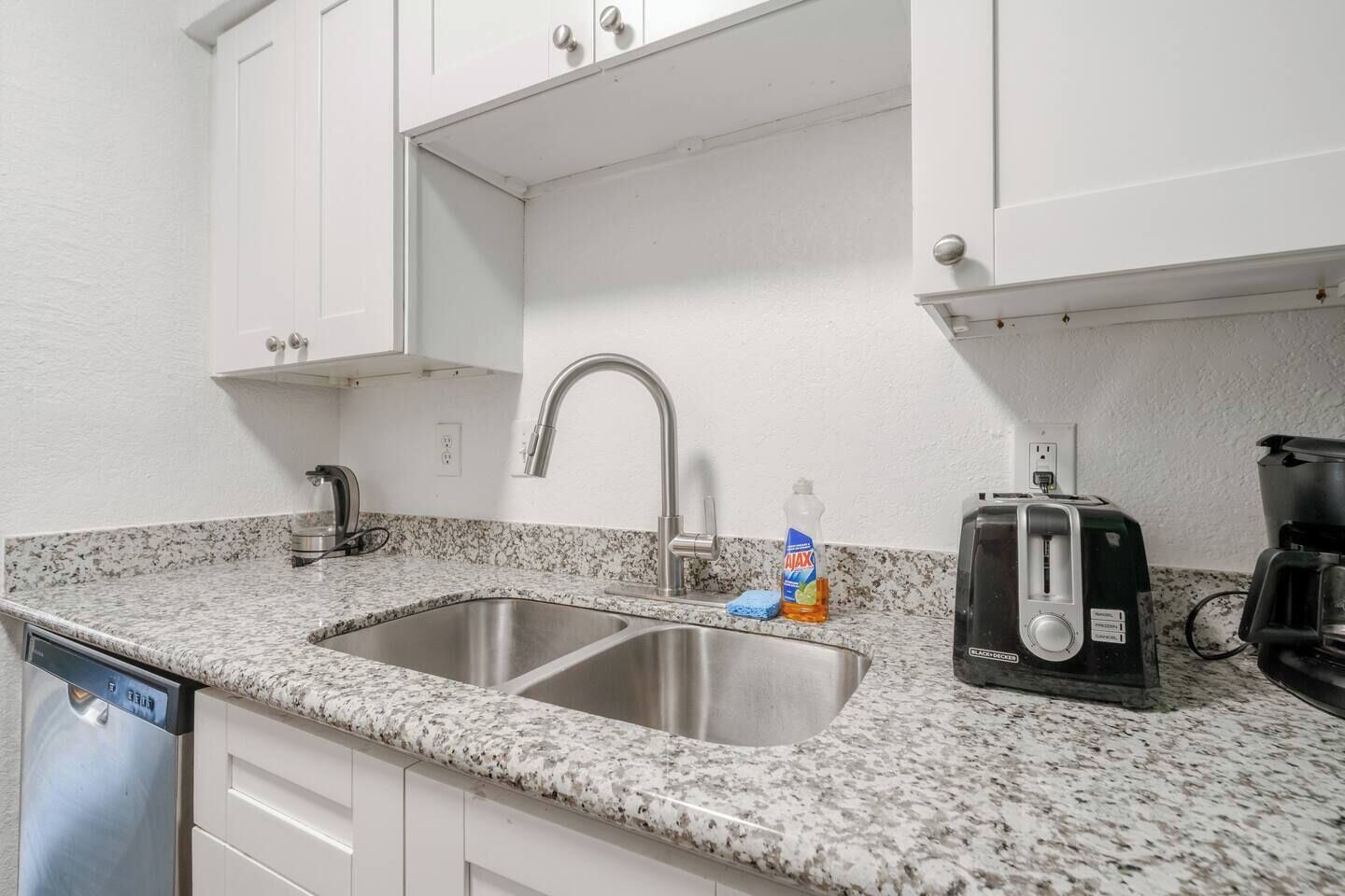 A kitchen with a granite countertop, stainless steel sink, white cabinets, a toaster, and a coffee maker.