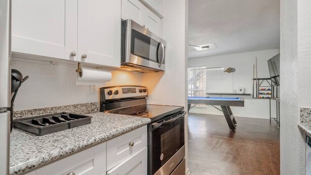 A modern kitchen with white cabinets, a stainless steel oven, a microwave, and a granite countertop. - Pool Table  Luxury 1Bed Apt in Downtown & Heights (Houston)