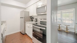 A kitchen with white cabinets, stainless steel appliances, and a wooden floor. - Pink 1BHK, 5 miles from Downtown + Free Parking (Houston)