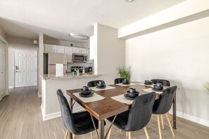 A modern kitchen with white cabinets, stainless steel appliances, and a dining area with a wooden table and black chairs.