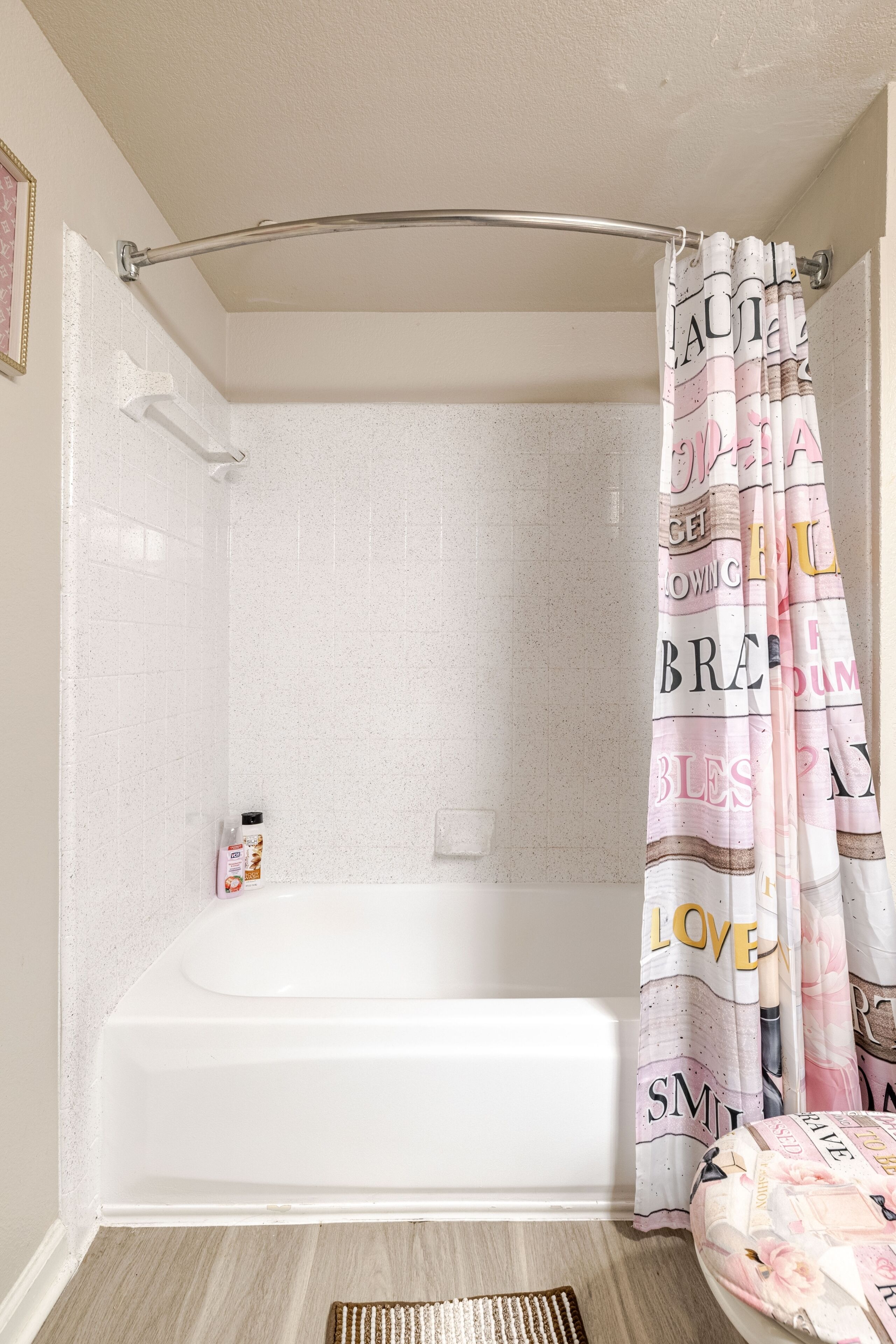 Un bagno con una vasca, una tenda da doccia con scritte e una piccola bottiglia sul pavimento.