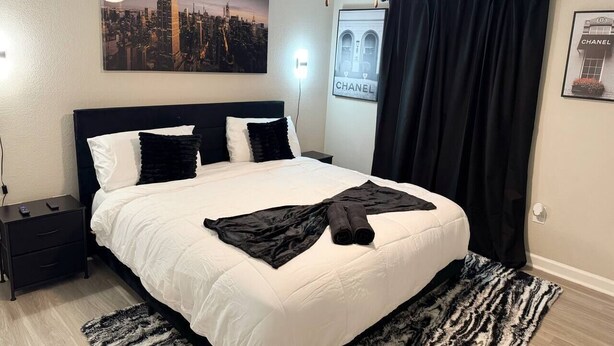 Ein Hotelzimmer mit einem Bett, einem Nachttisch, einer Wandleuchte, einem Deckenventilator und einem Stadtbild-Poster.