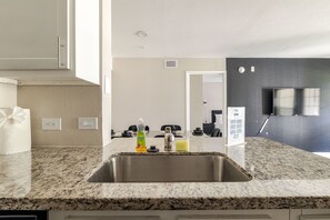 A modern kitchen with a granite countertop, stainless steel sink, and a dining area visible in the background.