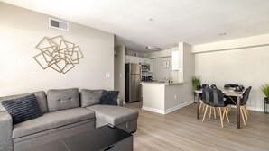 Ein modernes Wohnzimmer mit einem grauen Ecksofa, einem schwarzen Couchtisch und einem Essbereich mit Holztisch und Stühlen.