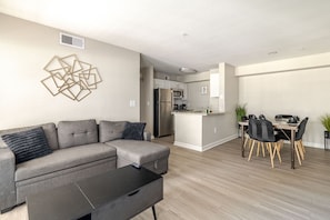 A modern living room with a grey sectional sofa, a black coffee table, and a dining area with a wooden table and chairs. - Gothic Blush King 2Bed near Texas Medical Center & in front of NRG Stadium (Houston)