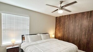 A bedroom with a large bed, a ceiling fan, a window with blinds, and a nightstand with a lamp. - Charming 3Bed 2Bath apt in front of NRG & near TMC (Houston)