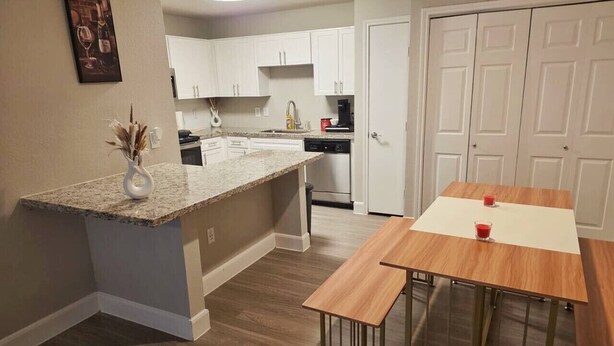 A modern kitchen with white cabinets, a granite countertop, and a wooden dining table. - Charming 3Bed 2Bath apt in front of NRG & near TMC (Houston)