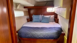 A compact, well-lit cabin with a bed featuring a quilted blue cover and two pillows labeled "Summer Time." A small window above the bed allows natural light. - Luxury 47’ Leopard Power Catamaran - Bahamas (Nassau)
