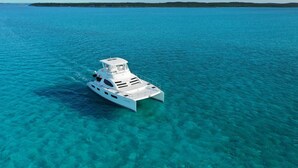 A white yacht on clear turquoise water with a flat roof and a cabin structure. - Luxury 47’ Leopard Power Catamaran - Bahamas (Nassau)