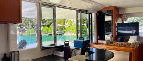 A compact kitchen with a sink, a small refrigerator, and a window offering a view of a pool and greenery.