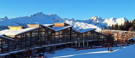 A ski resort with wooden buildings, snow-covered slopes, and mountains in the background.