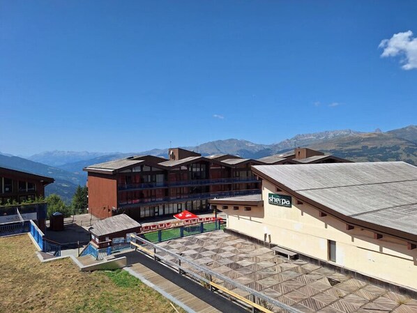 Un hôtel à étages, une enseigne indiquant « Sherpa », et une vue sur les montagnes en arrière-plan.