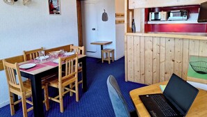 Ein gemütliches Zimmer mit Esstisch, Stühlen, einem Laptop und einer Küchenzeile mit Mikrowelle und Toaster.