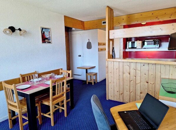 Une pièce confortable comprenant une table à manger, des chaises, un ordinateur portable et une kitchenette équipée d’un four à micro-ondes et d’un grille-pain.
