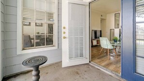 Ein Zimmer mit einer Schiebetür zum Glasbalkon, einem kleinen Tisch und einer Essecke mit einem Stuhl und einer Pflanze.
