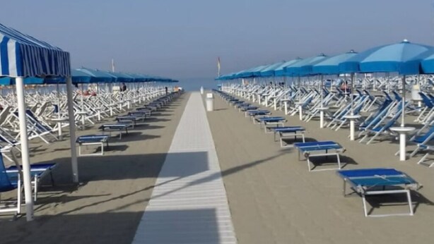 A beach with rows of sun loungers and umbrellas, a clear sky, and a pathway leading to the water. - Cozy Rustico for 6/7 people with umbrella in Lido di Camaiore (Camaiore)