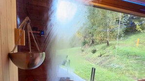 A traditional Japanese onsen with a wooden interior, a stone hot spring bath, and a view of a green landscape through a large window.
