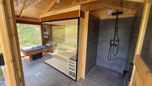 A wooden cabin with a glass-enclosed massage area, a shower, and a bench with towels.