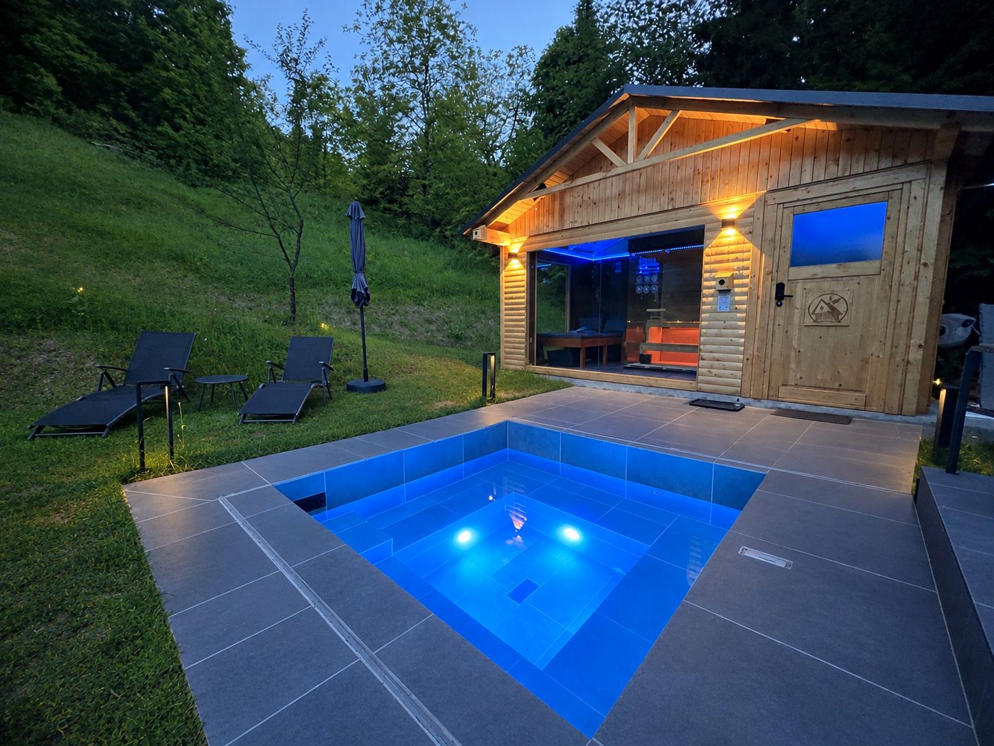 A wooden cabin with a swimming pool, outdoor seating, and a glass door entrance.