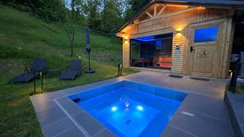 A wooden cabin with a swimming pool, outdoor seating, and a glass door entrance.