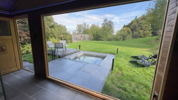 A modern outdoor patio with a hot tub, a dining area, and a grassy lawn.
