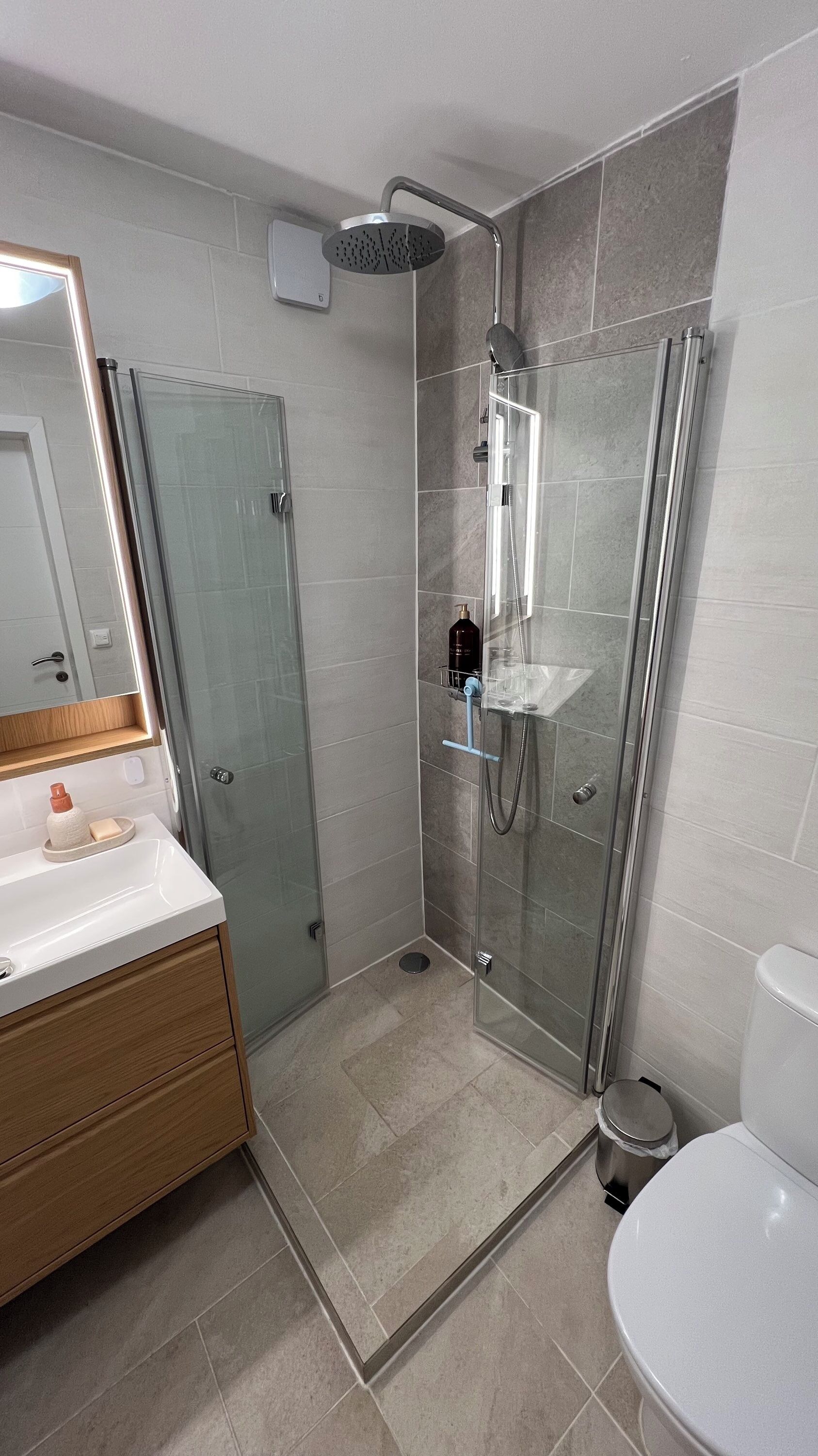 Un baño moderno con ducha envuelta en vidrio, tocador de madera y un inodoro blanco.
