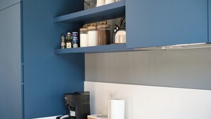 A modern kitchen with blue cabinetry, a coffee maker, and storage jars on the shelves.